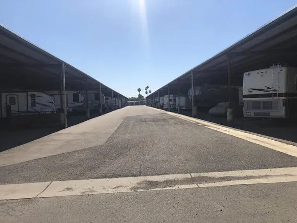 Outdoor covered parking area with recreational vehicles and trailers parked along a paved asphalt driveway