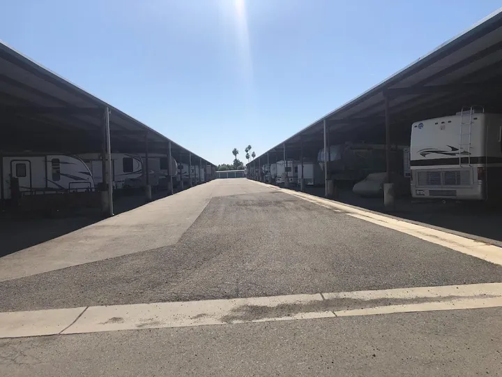 Outdoor covered parking area with recreational vehicles and trailers parked along a paved asphalt driveway
