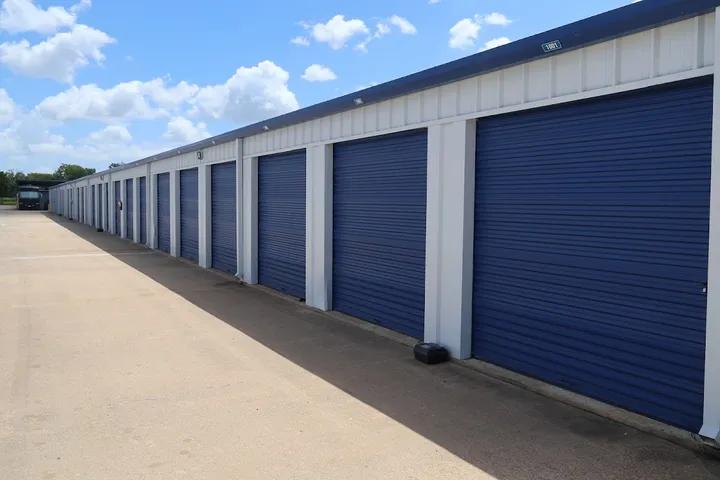 Exterior row of white drive-up storage units with blue roll-up doors and a concrete driveway