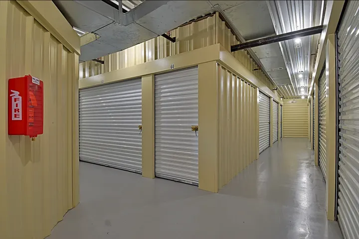 Indoor self-storage hallway featuring beige corrugated walls, white roll-up doors, and a red fire extinguisher cabinet