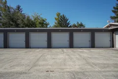 A row of drive-up self-storage units with white roll-up doors and numbered dark gray brick exteriors