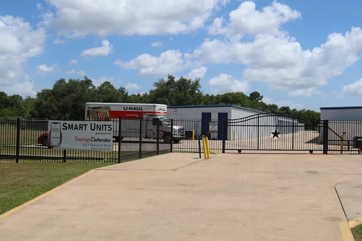 A gated entrance to a storage facility with a U-Haul truck parked near white storage buildings