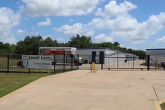 A gated entrance to a storage facility with a U-Haul truck parked near white storage buildings