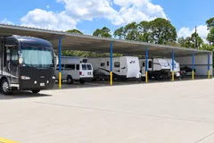 Several motorhomes and a white van parked in a covered outdoor storage area with blue pillars
