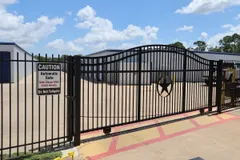 Black metal sliding security gate with a star emblem in front of storage buildings and paved driveways