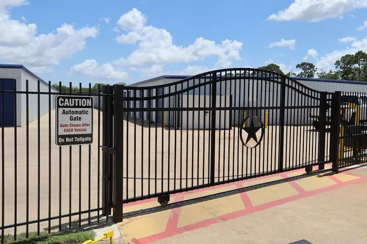 Black metal sliding security gate with a star emblem in front of storage buildings and paved driveways