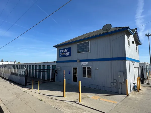 A two-story Purely Storage leasing office beside a gated entrance and rows of outdoor storage units