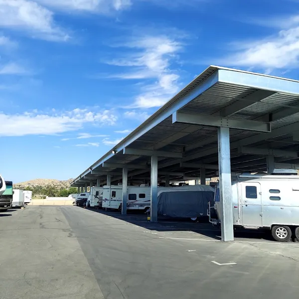 Row of recreational vehicles and trailers parked under a metal canopy in an outdoor storage lot