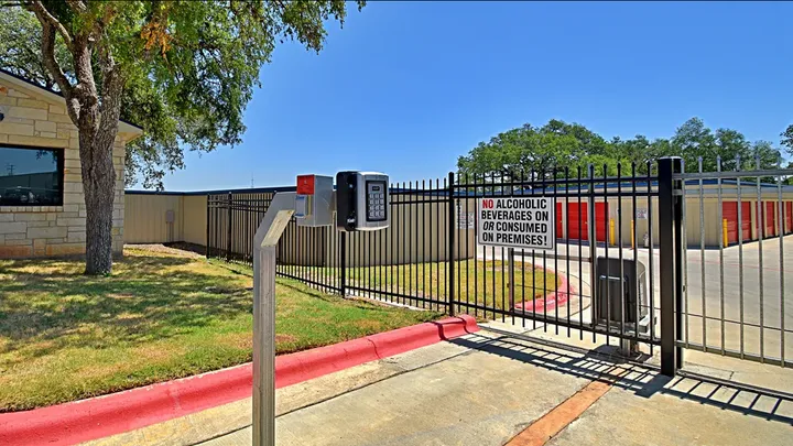 Security keypad and gated entrance to a storage facility with red roll-up doors in the background