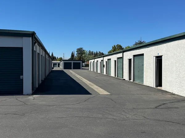 Rows of drive-up storage units with dark green roll-up doors and paved drive aisles under a clear sky