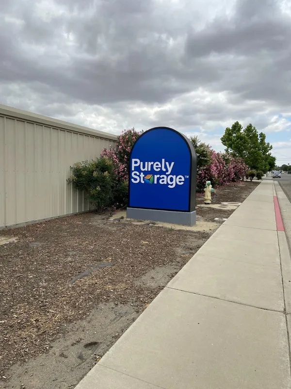 Blue Purely Storage monument sign next to pink flowering bushes and a tan metal facility wall
