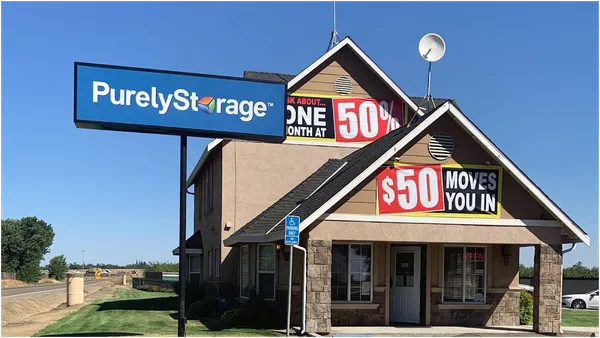 A two-story leasing office with stone accents featuring Purely Storage signage and promotional banners under a blue sky
