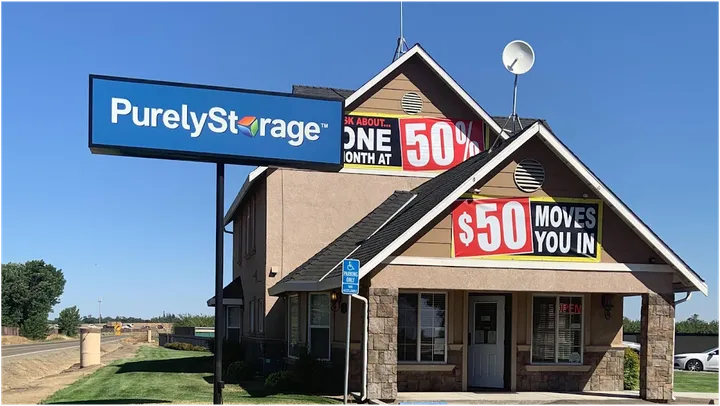 A two-story leasing office with stone accents featuring Purely Storage signage and promotional banners under a blue sky