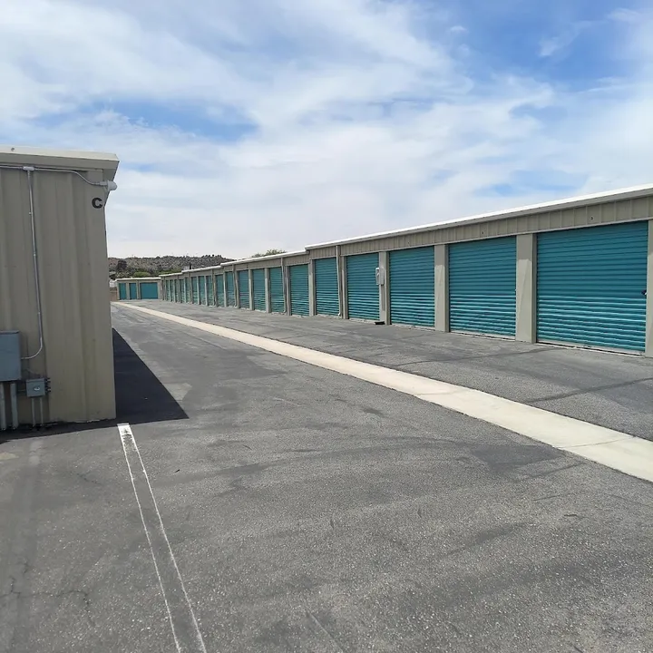 Outdoor self-storage facility featuring long rows of tan buildings with teal roll-up metal doors
