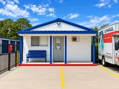 White and blue storage rental office with a bench and a U-Haul truck parked nearby