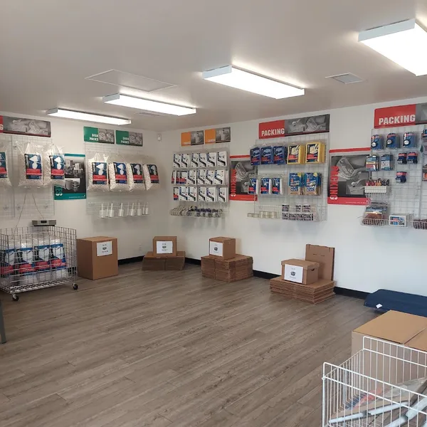 A bright storage facility office featuring cardboard boxes and various packing supplies displayed on wire wall racks