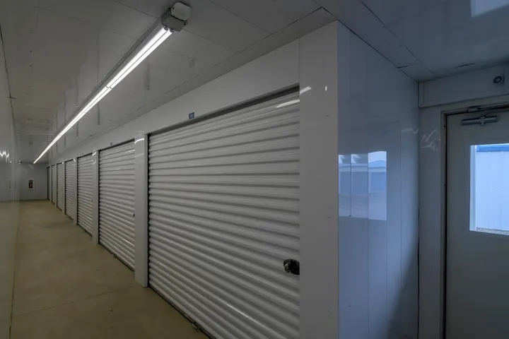 Well lit indoor hallway with a row of white corrugated roll up storage unit doors