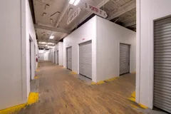 Indoor storage facility hallway with white units, grey roll-up doors, and wooden floors under hanging street signs