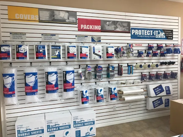 A slatwall retail display featuring packing supplies, bubble wrap, furniture covers, tape, and boxes for sale