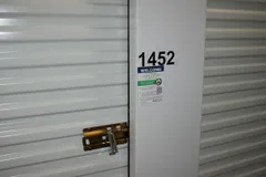 A white corrugated storage unit door featuring a gold latch, silver lock, and the number 1452