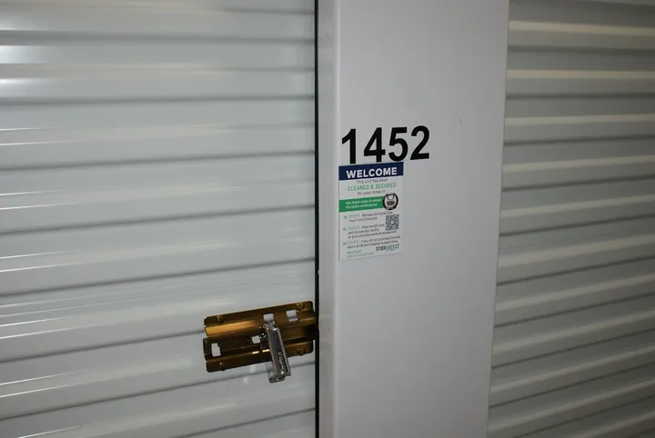 A white corrugated storage unit door featuring a gold latch, silver lock, and the number 1452