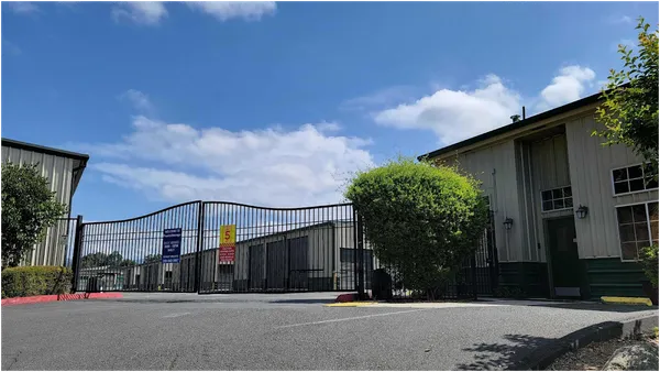 Black wrought iron security gates and a tan office building at a self-storage facility entrance