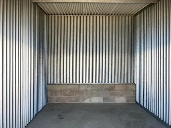 Interior view of an empty storage unit with corrugated metal walls and a cinder block base