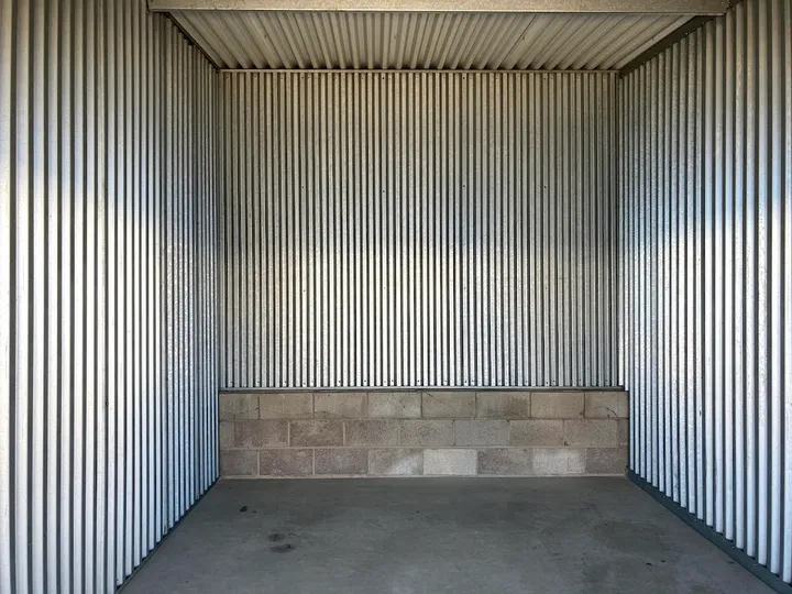 Interior view of an empty storage unit with corrugated metal walls and a cinder block base