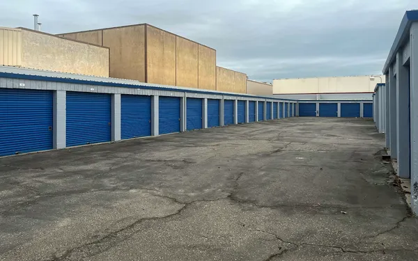 Outdoor drive-up self-storage facility featuring long rows of blue roll-up doors and a paved asphalt lot