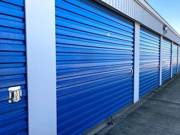 Row of blue drive-up storage unit doors with white trim and metal latches along a concrete path