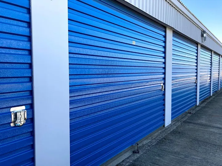 Row of blue drive-up storage unit doors with white trim and metal latches along a concrete path