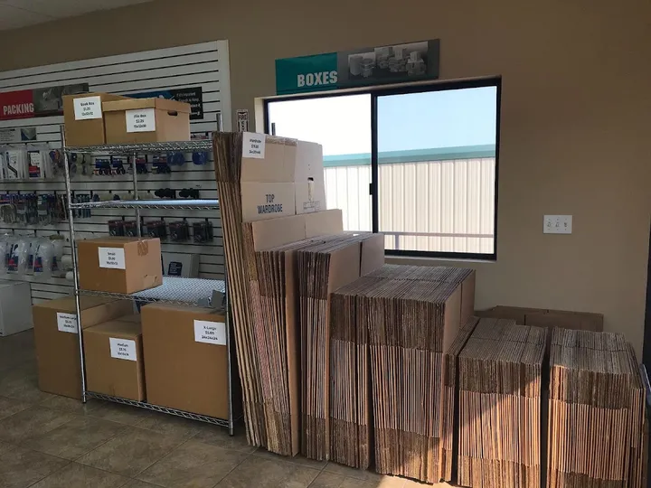 A storage facility office featuring metal shelving and stacks of cardboard moving boxes for sale