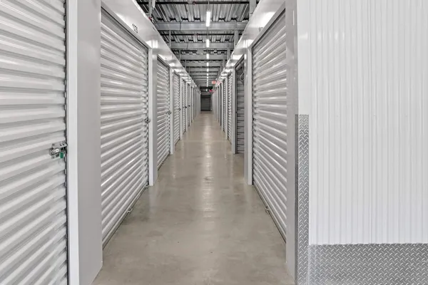 Indoor storage facility hallway with white roll-up doors, concrete floors, and overhead fluorescent lighting
