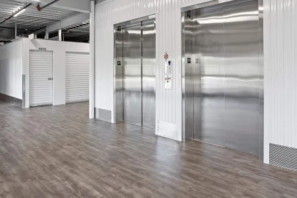 Indoor storage facility hallway featuring two stainless steel elevators next to white roll-up unit doors