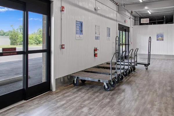 Indoor loading area with several moving carts lined up along a white corrugated wall by glass doors