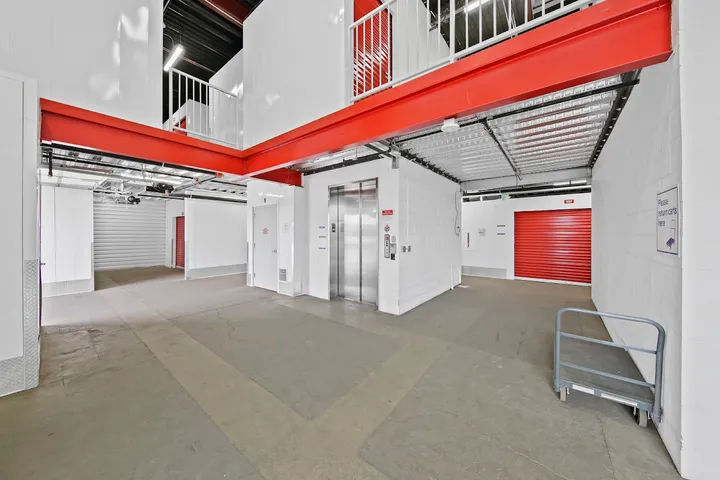 Interior hallway with security cameras, elevator, and red unit doors