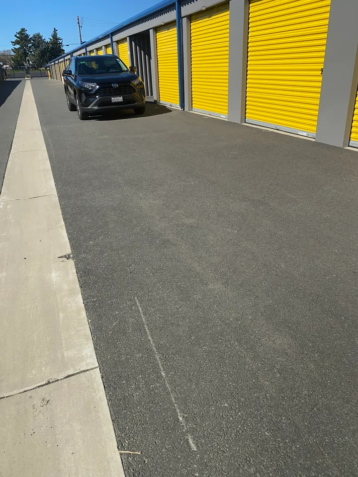 Driveway past outdoor storage units with yellow doors; car parked.