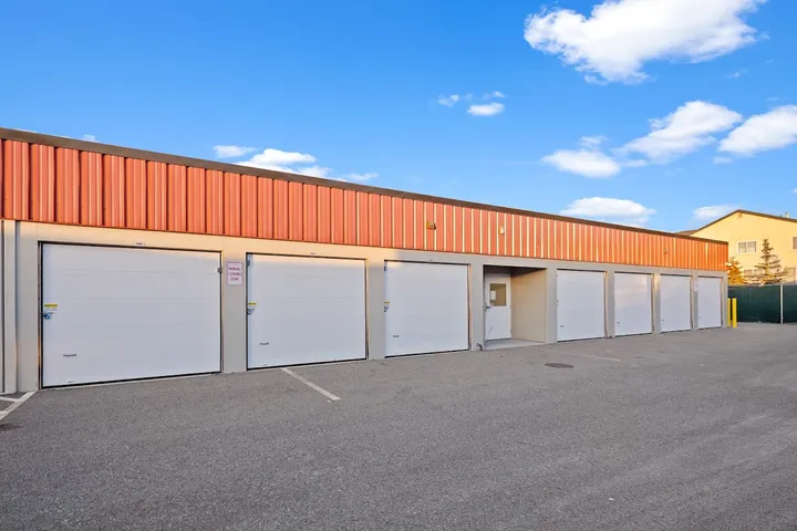 Exterior of storage units with white unit doors and parking spaces.