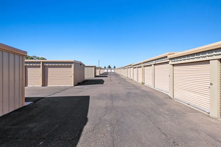Outdoor storage units with roll-up doors along a paved driveway.