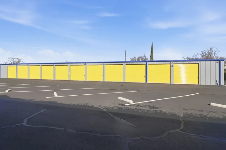 Parking lot view of drive-up storage units with yellow doors.