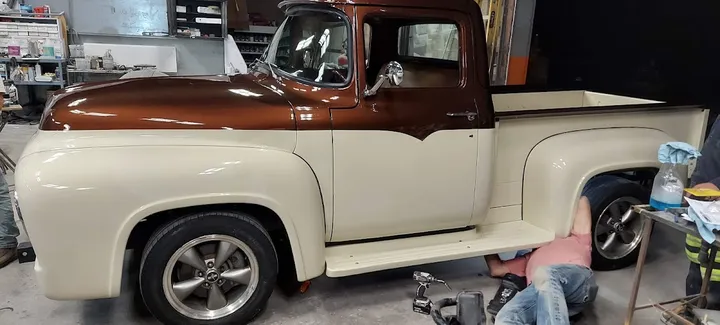 Classic Ford pickup truck being worked on by mechanics.