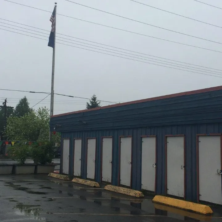 Outdoor self-storage building with blue siding and white unit doors next to an American flag