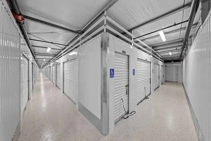Well-lit interior hallway with rows of white storage unit doors.
