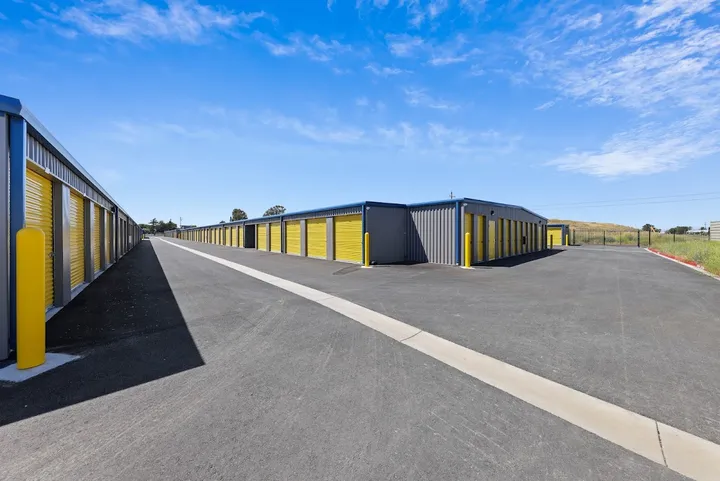 Long driveway between rows of outdoor storage units with yellow doors.