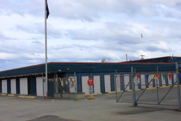 A blue storage building with white unit doors behind a chain-link fence with colorful pennant flags