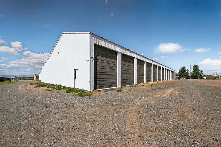 A row of white drive-up storage units in Laramie, WY, with large dark gray roll-up doors on gravel ground