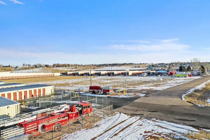 Wide view of the storage facility with buildings, roads, and parked fire truck.