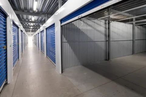 Indoor storage hallway featuring rows of blue roll-up doors and a large open unit with corrugated walls