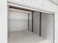 Interior of an empty self-storage unit with corrugated metal walls and concrete flooring under a raised door