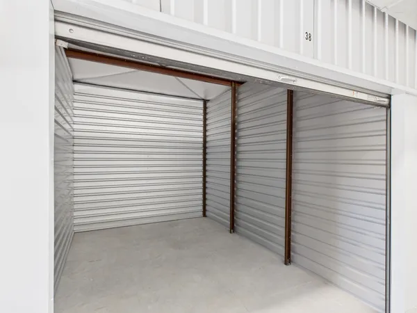 Interior of an empty self-storage unit with corrugated metal walls and concrete flooring under a raised door